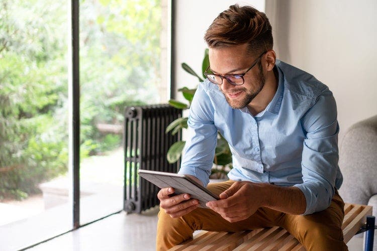 A smiling person sitting on a bench using a tablet to remove redactions from a PDF.