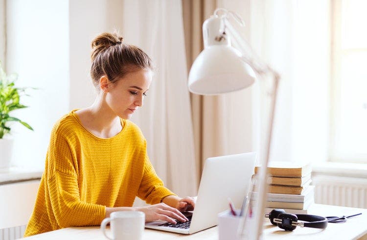 A young woman in a yellow blouse working in a brightly lit room to create a fillable PDF on a Mac.