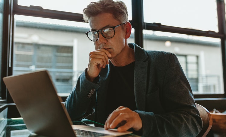 A man sitting at a table uses his laptop to extract images from a PDF document