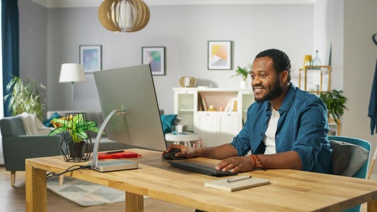 A man uses a Windows 10 monitor, keyboard, and mouse to type and write on PDF files from a home office.
