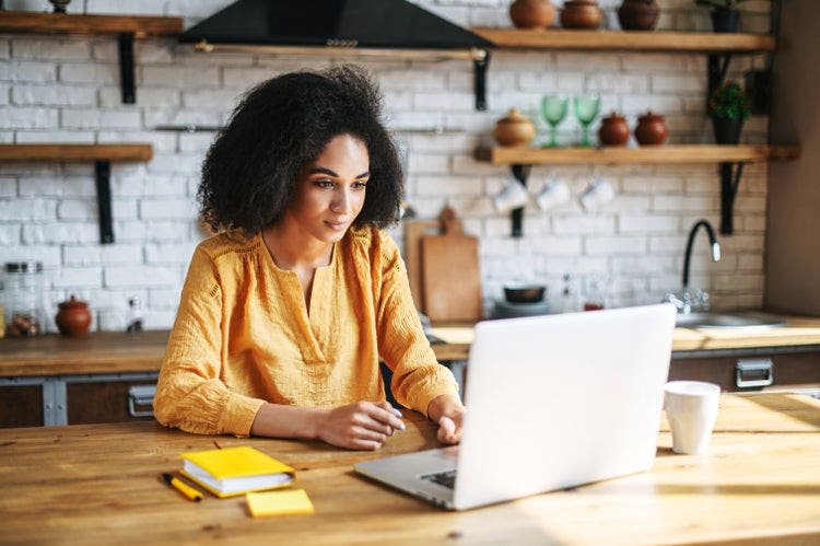 A woman sitting at a kitchen counter reads a PDF file using a Mac laptop.