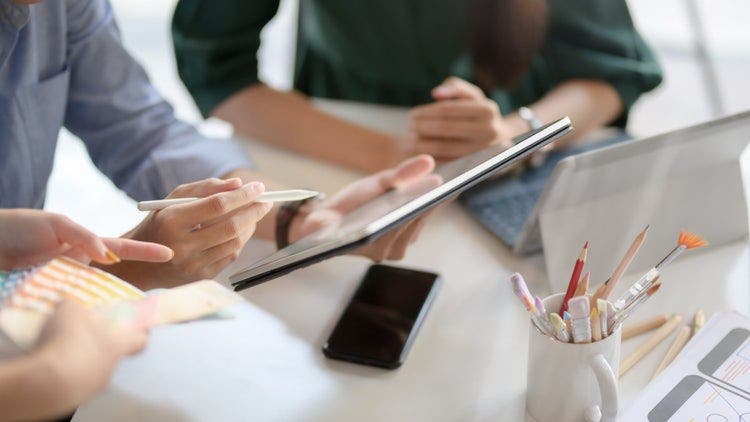 A man uses a stylus and an iPad to highlight a PDF file in a meeting with two co-workers.