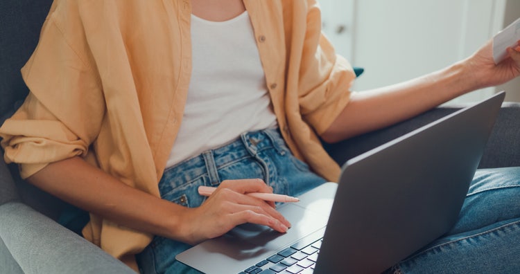 A woman on a couch with a laptop categorizing her to-do list for work.