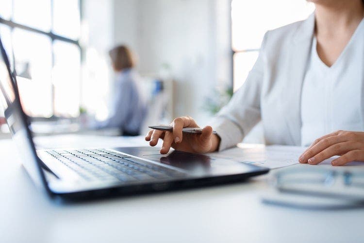 A woman sitting at a desk in an office uses a laptop to remove her signature from a PDF.