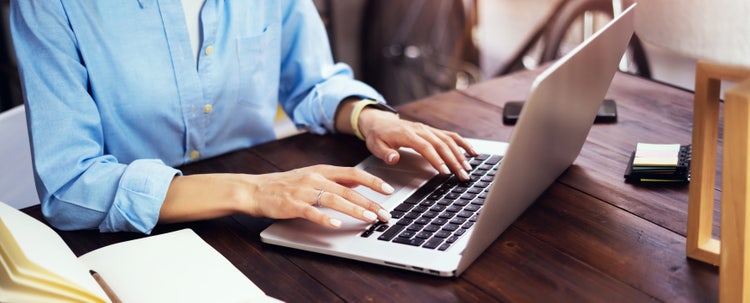 A person using a laptop to access and edit an RTF file on a wooden table.