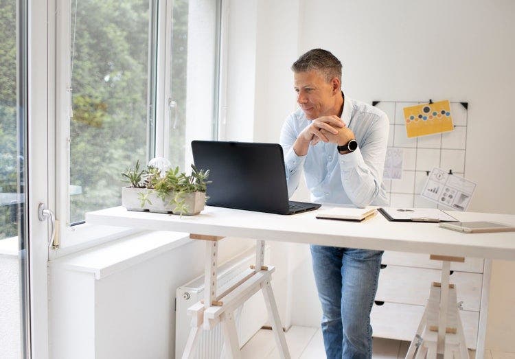 A man stands over a desk looking at his laptop.