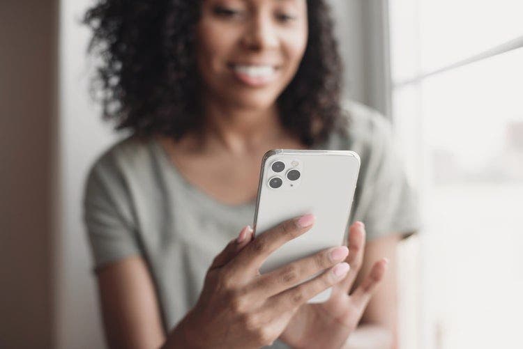 A woman near a window reads a PDF file on an iPhone.