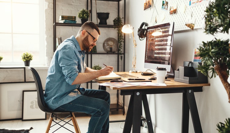 A person taking notes in their notebook while sitting in front of their desk.