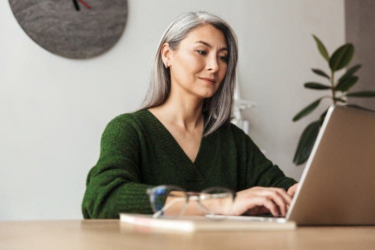 A woman sits at a table to combine Word documents on her laptop.