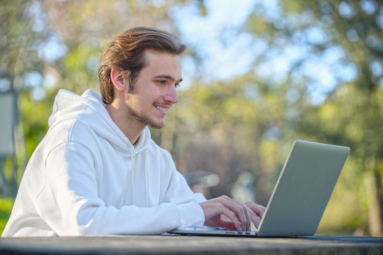 A man sitting outside uses his laptop to write a mobile home bill of sale.