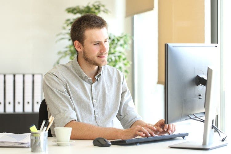 A man sitting at his desk redacts a PDF on his PC.