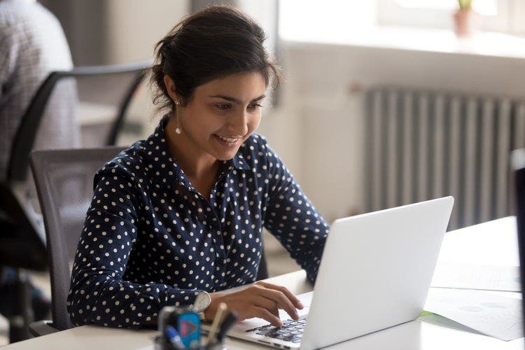 A woman sitting at a desk deletes pages from a PDF on a Mac laptop.