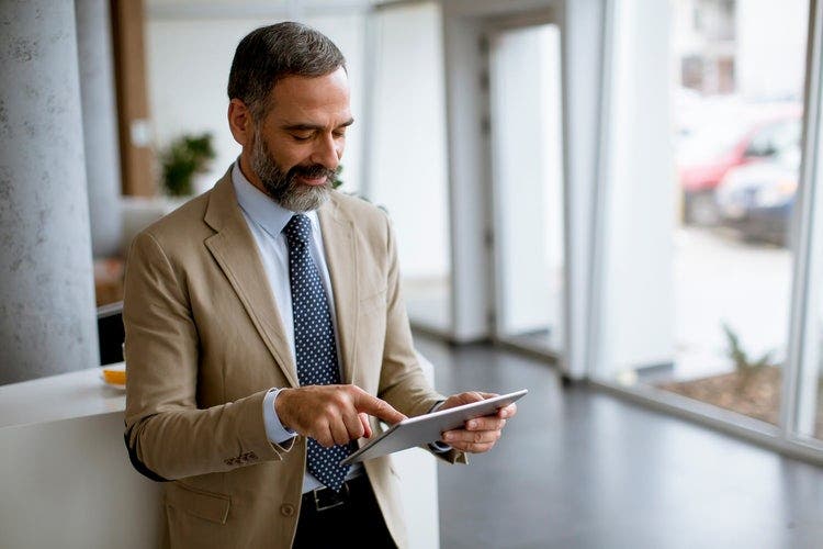 A business professional standing near a window updates his iPad settings to allow the device to read PDFs aloud.