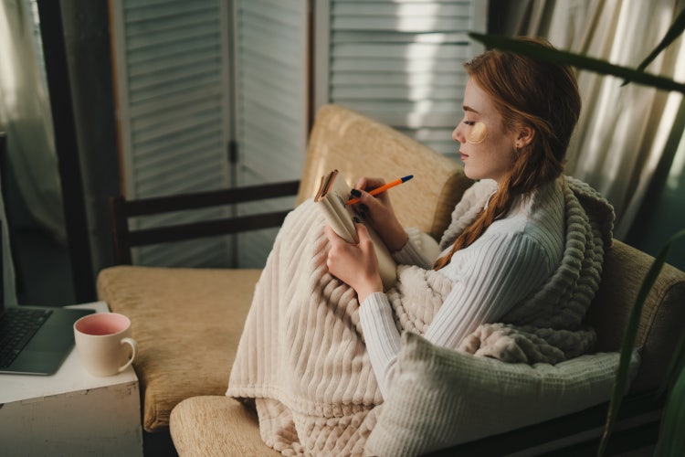 A woman in a living room creates a self-care checklist.