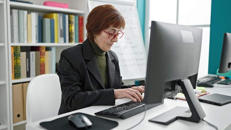 A teacher manages student report cards online using her desktop computer.
