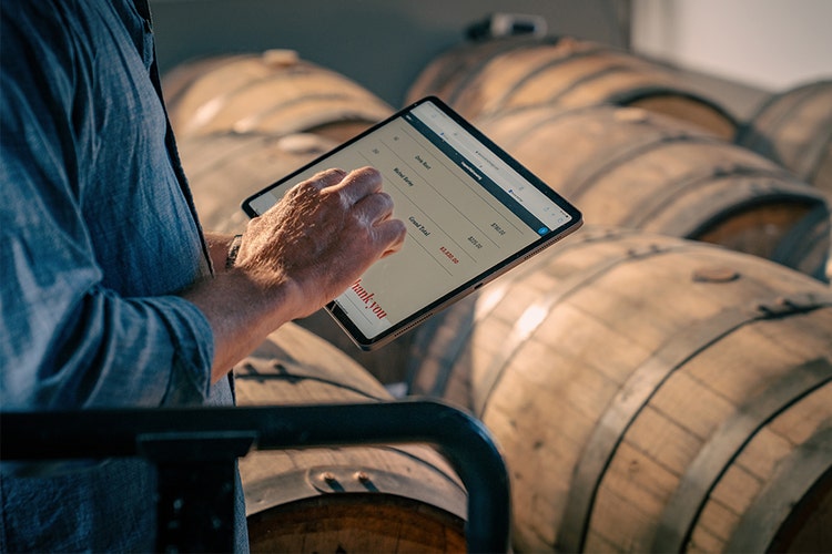 Person wearing a denim shirt overlooking wooden distillery casks and barrels editing a scanned PDF invoice on a tablet.