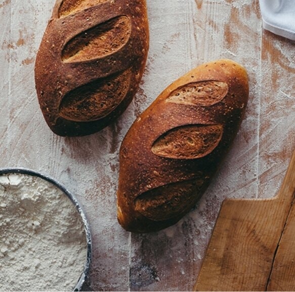 To the left: Two loaves of bread with scored crust on a flour-laden table.
