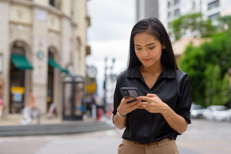 A woman standing outside uses an Android phone to type on a PDF.