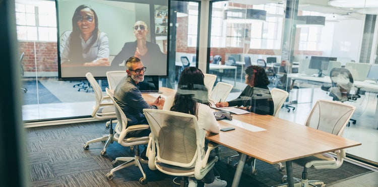 A global team meets together both in person and online in a conference room.