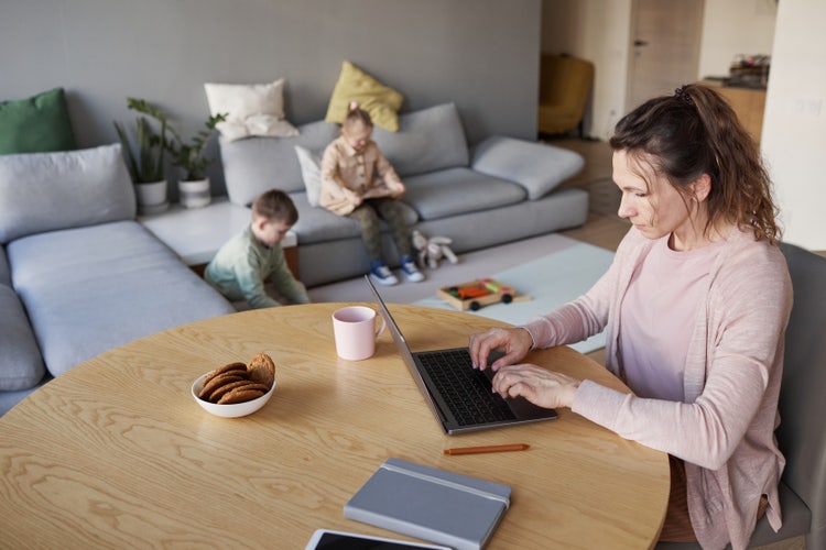 A woman writing a parental consent form while in the living room with her kids.