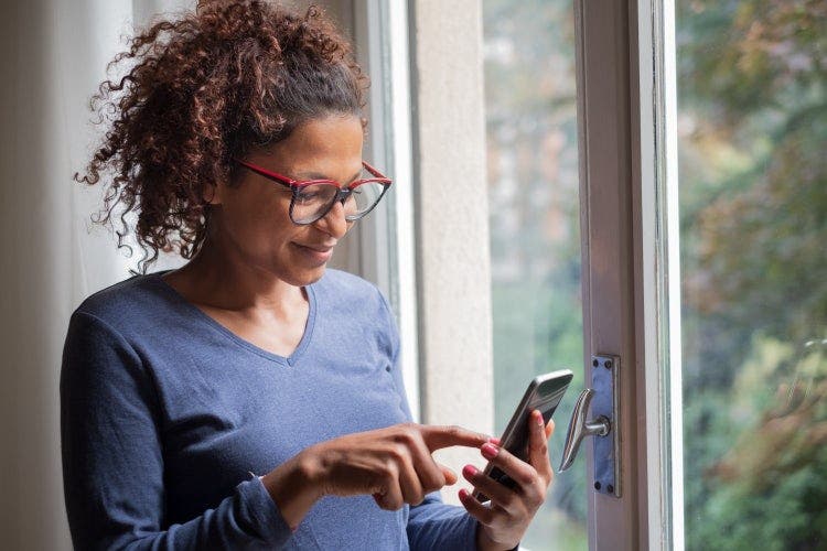 A woman standing near a window uses an iPhone to draw on a PDF.