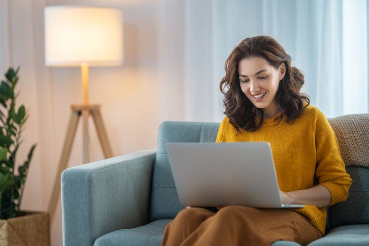 A woman sitting on a couch using a laptop to convert GIF images to PDF.