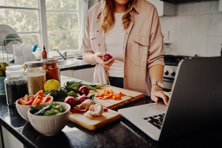 A woman uses her laptop in the kitchen to organize recipes by category.