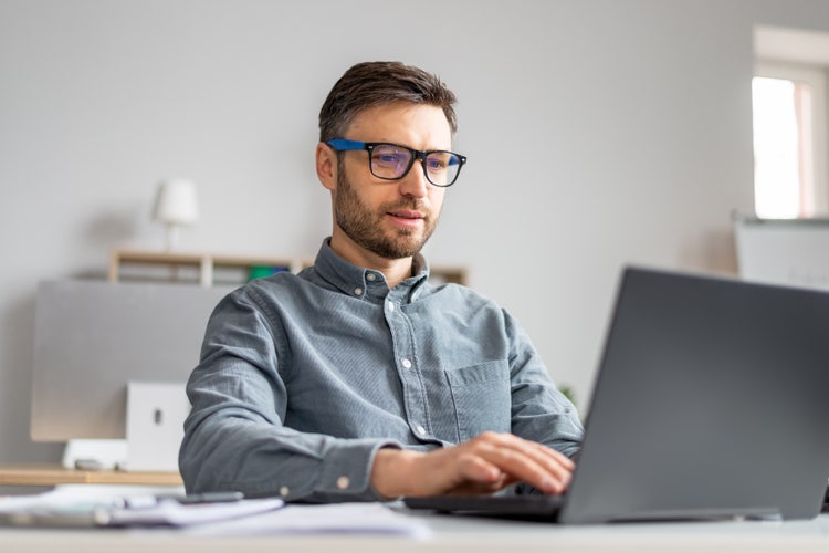A man using a laptop to compare Excel and Google Sheets.