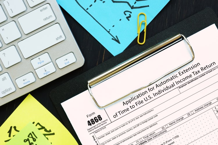 Form 4868 is shown on a clipboard next to a keyboard and sticky notes on a table.