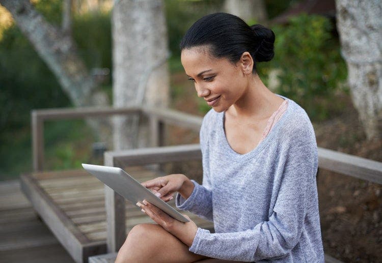 A woman sitting outside on a bench uses an iPad to type on a PDF file.