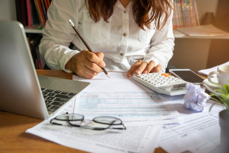 Printed tax forms are filled out with the help of a calculator and laptop.