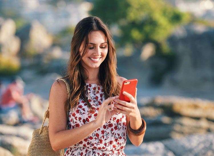 A woman standing outside uses a phone to create a social media plan template.