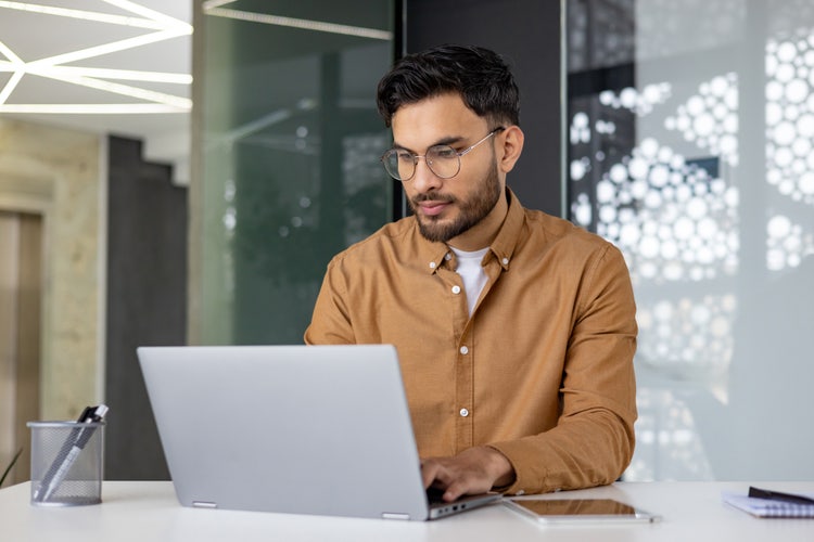 A man sitting at a table types on his laptop.