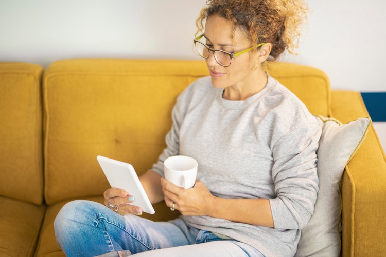 A woman sitting on a yellow couch reads a MOBI file on her white tablet device.