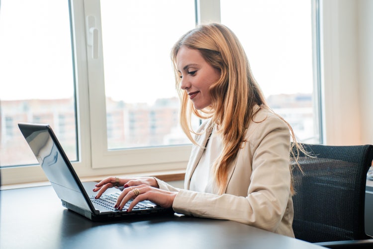 A woman with a tan business coat and blonde hair sits at a desk and uses her computer to view and edit an ASC file.