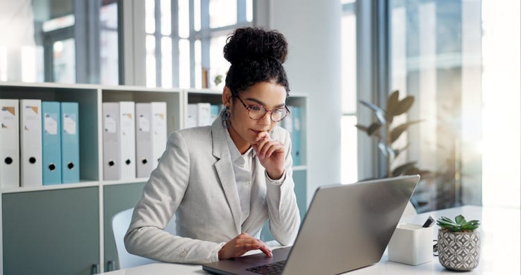 A woman sitting at a desk creates a .DOC file on her laptop computer.