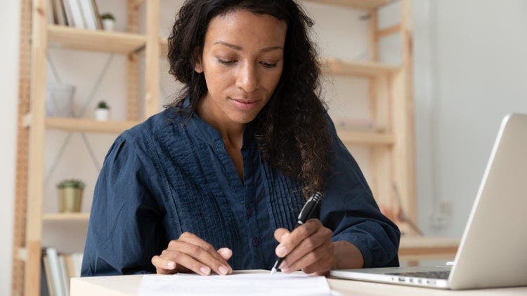 A woman sitting at a desk writes with a pen on a piece of paper.