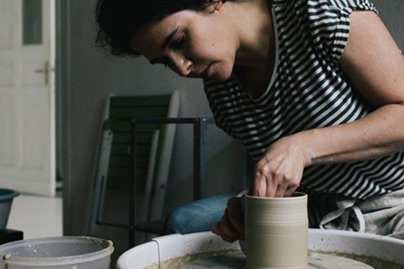 A potter sitting on a stool making a clay pot on a pottery wheel