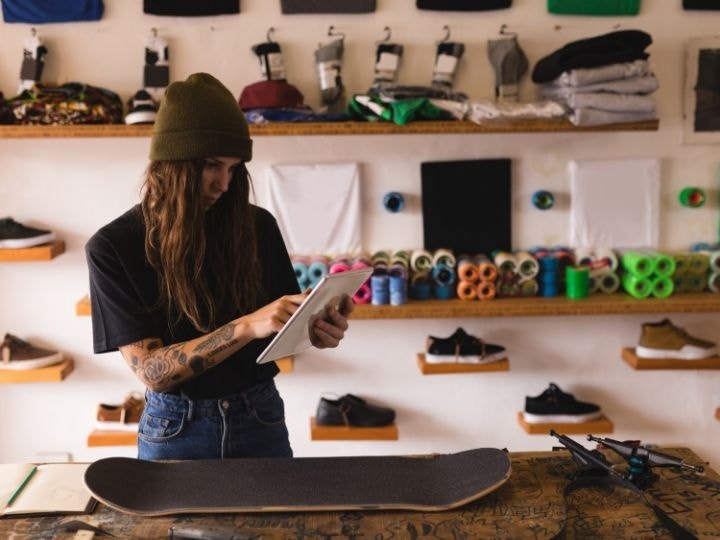 A skateboard shop owner standing in their workshop putting together an order form for more parts using a tablet with Adobe Acrobat