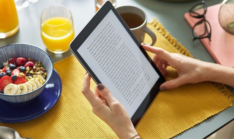 Close-up on the hands and tablet of a person who is reading an eBook at the breakfast table while their food goes slightly ignored