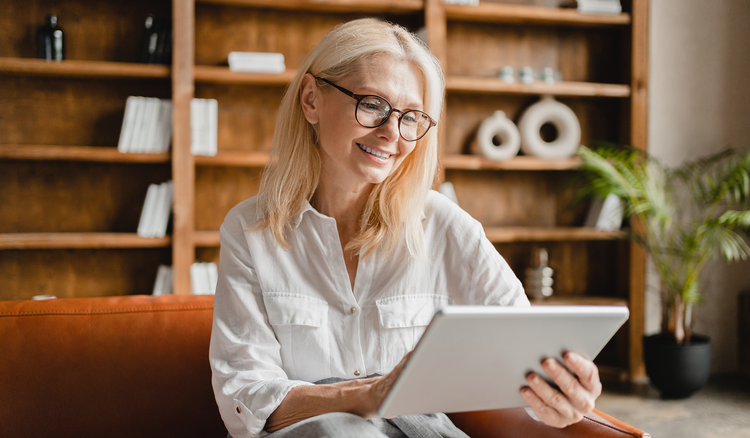 Woman sits on a couch and makes a daily schedule on a tablet.