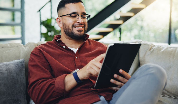 A man sitting on a couch looks at a tablet device.