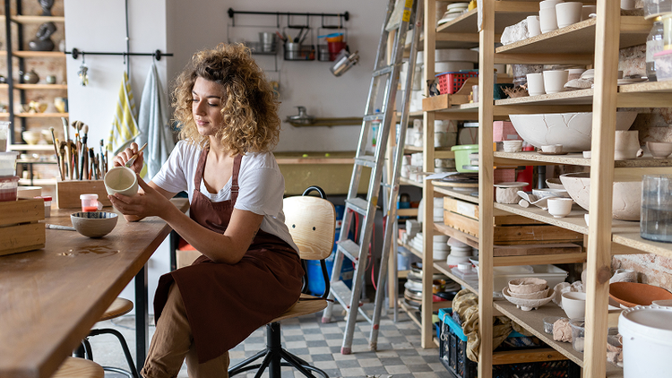 A woman in a pottery studio sits at a table holding a cup.