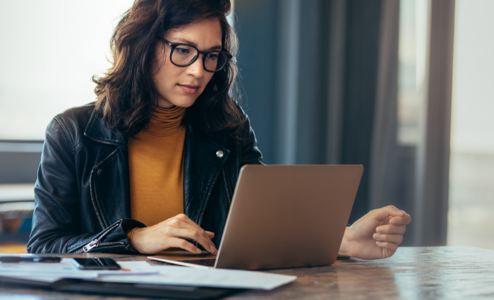 A woman sitting at a desk looks at a laptop.