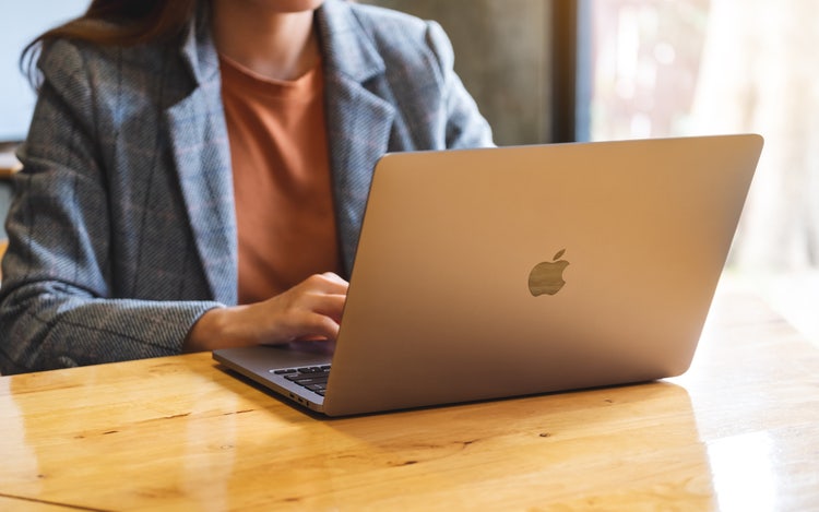 A woman in a blazer sitting at a desk works on a MacBook computer to add a signature in Pages.