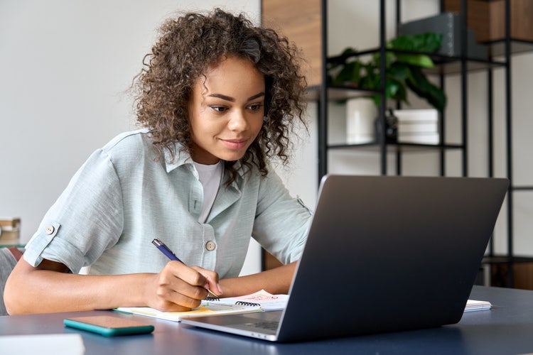 A photo of a person sitting at a table and taking notes for their thesis statement.