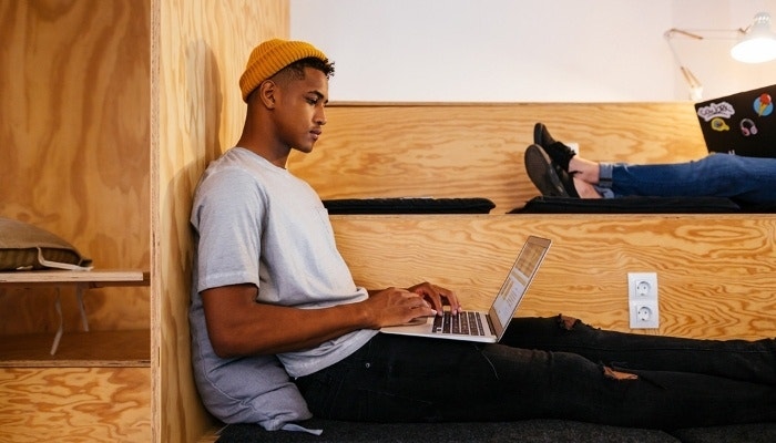 Students lounge on large plywood steps while taking digital notes on their laptops
