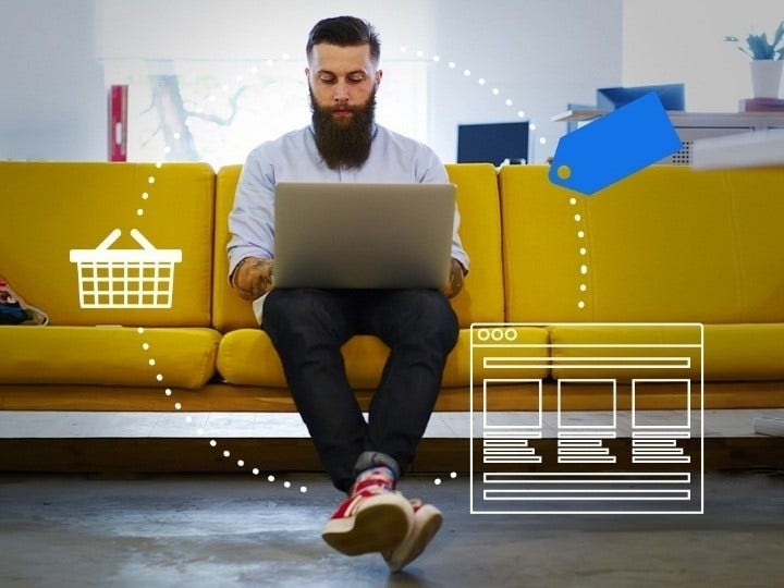 A man with a beard sits on a couch while starting an online business from his laptop.
