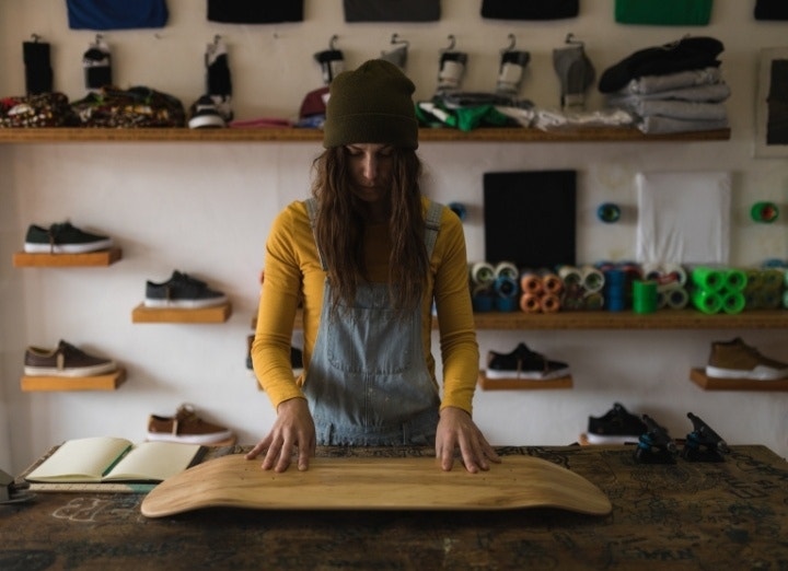 A skateboard shop owner looking over a blank skateboard deck on a workbench in their workshop