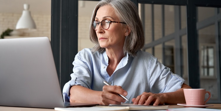A woman wearing glasses writes notes while researching how PDF software can help edit files.